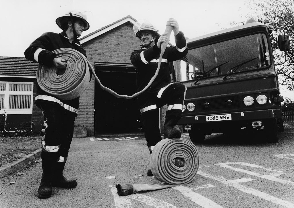 Firemen checking hose reels in front of fire engine