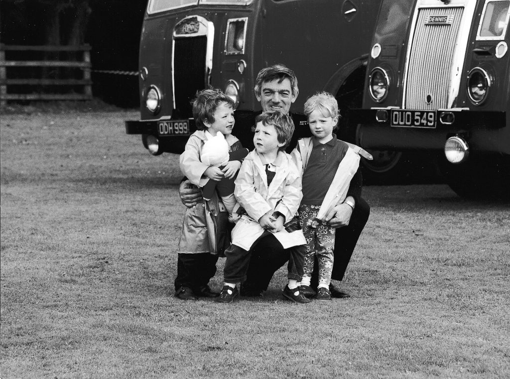 Three children with their father in front of two fire engines